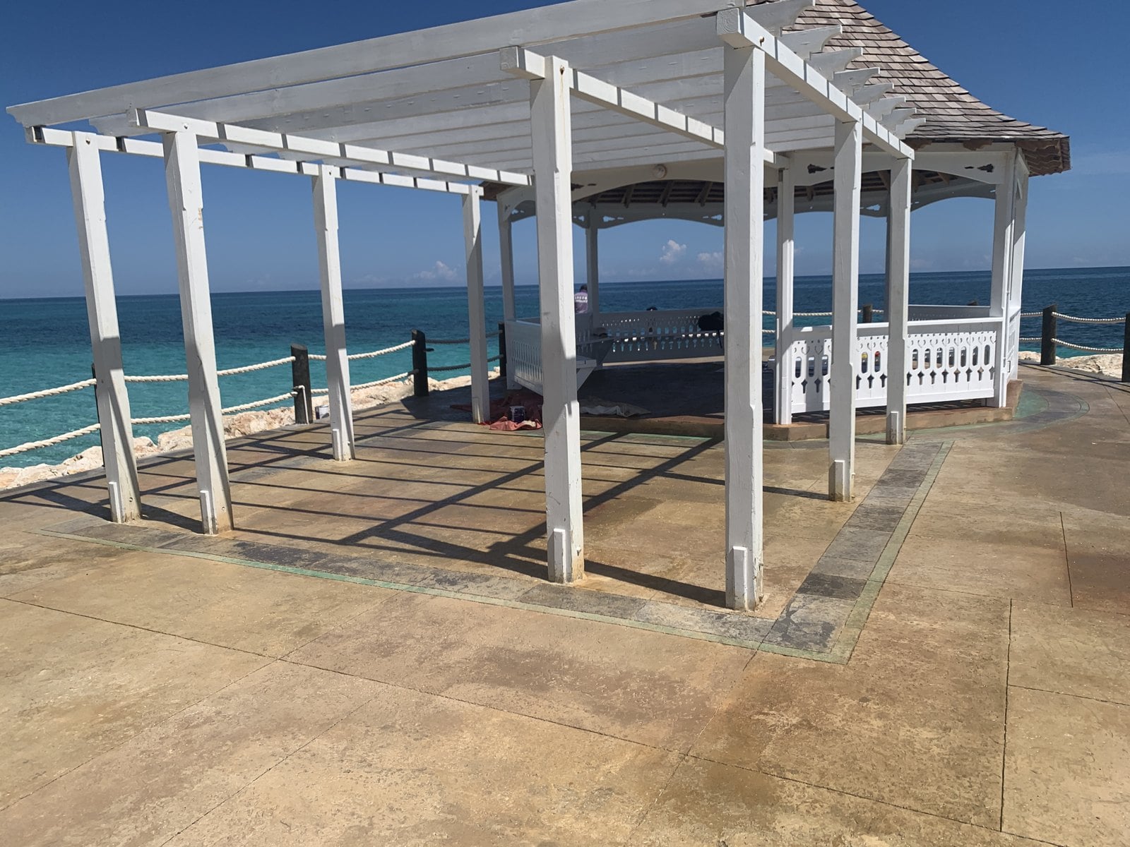 Decorative paving around a white seaside gazebo, with strong sun and the sea beyond
