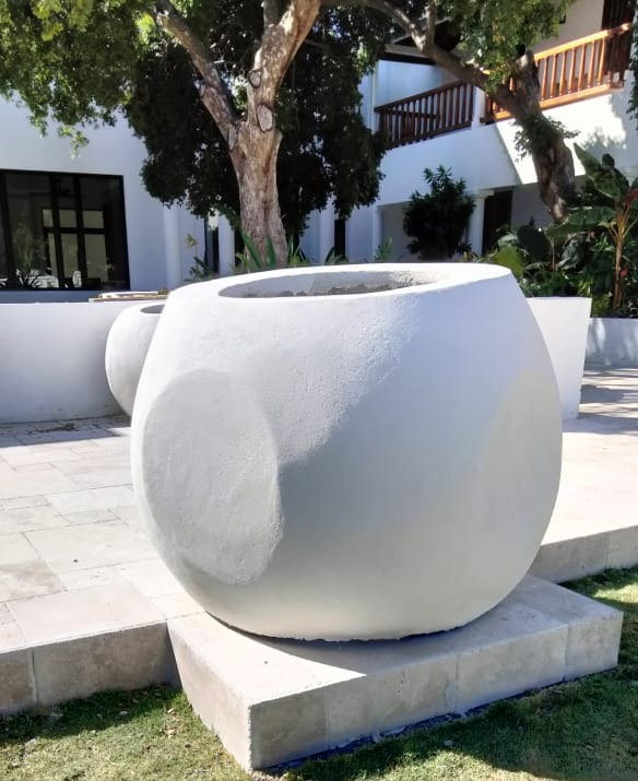 Oversized white sculptural concrete planters positioned on individual plinths in the courtyard, with the second planter farther back
