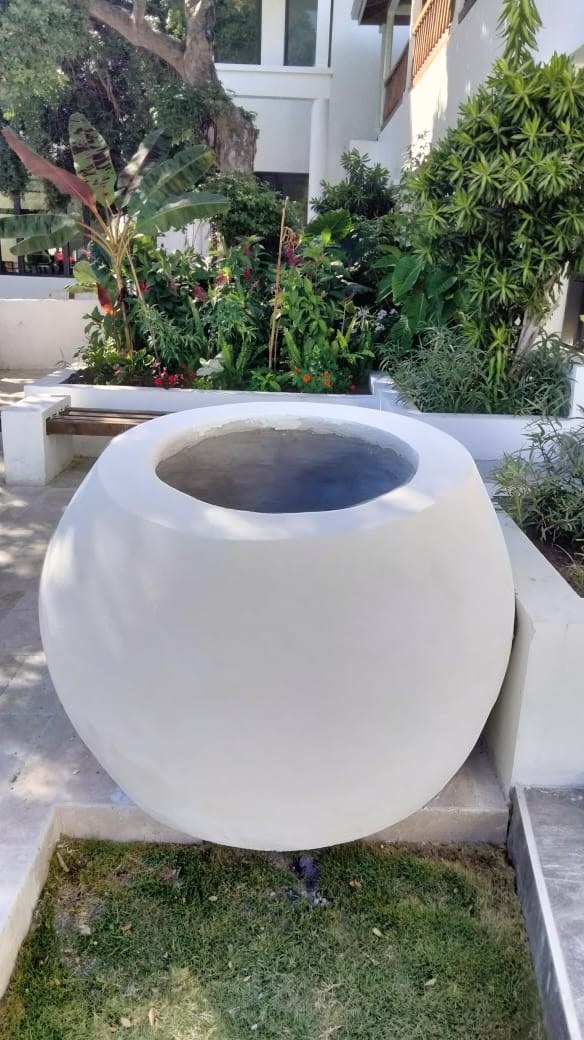 A rounded white concrete planter on its own plinth beside the planted edge of the EU courtyard