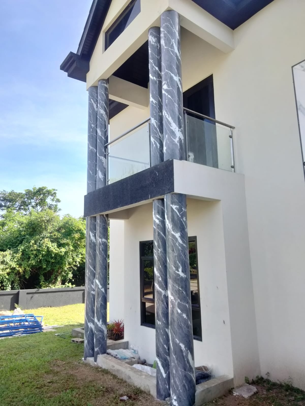 Black-and-white marble-effect Venetian plaster columns framing a villa balcony, with glass balustrades and cream walls.