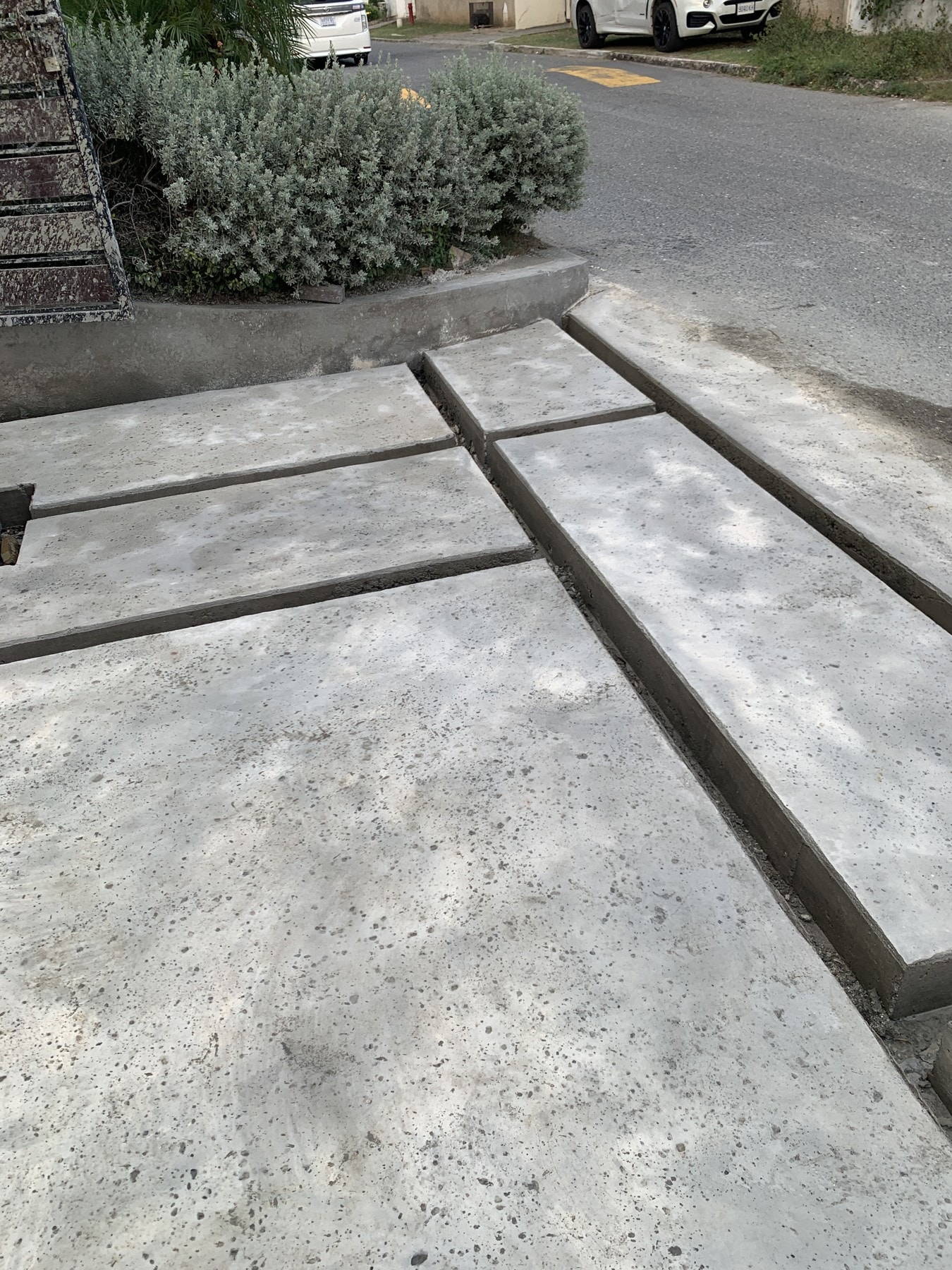 Rocksalt-textured slabs and open joints meet the planted entrance, with rounded edges softening the layout.