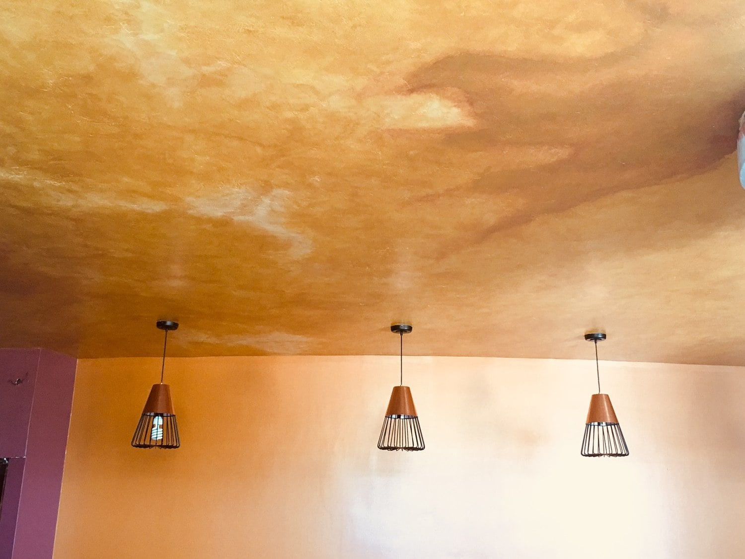 Warm gold decorative ceiling above three pendant lights