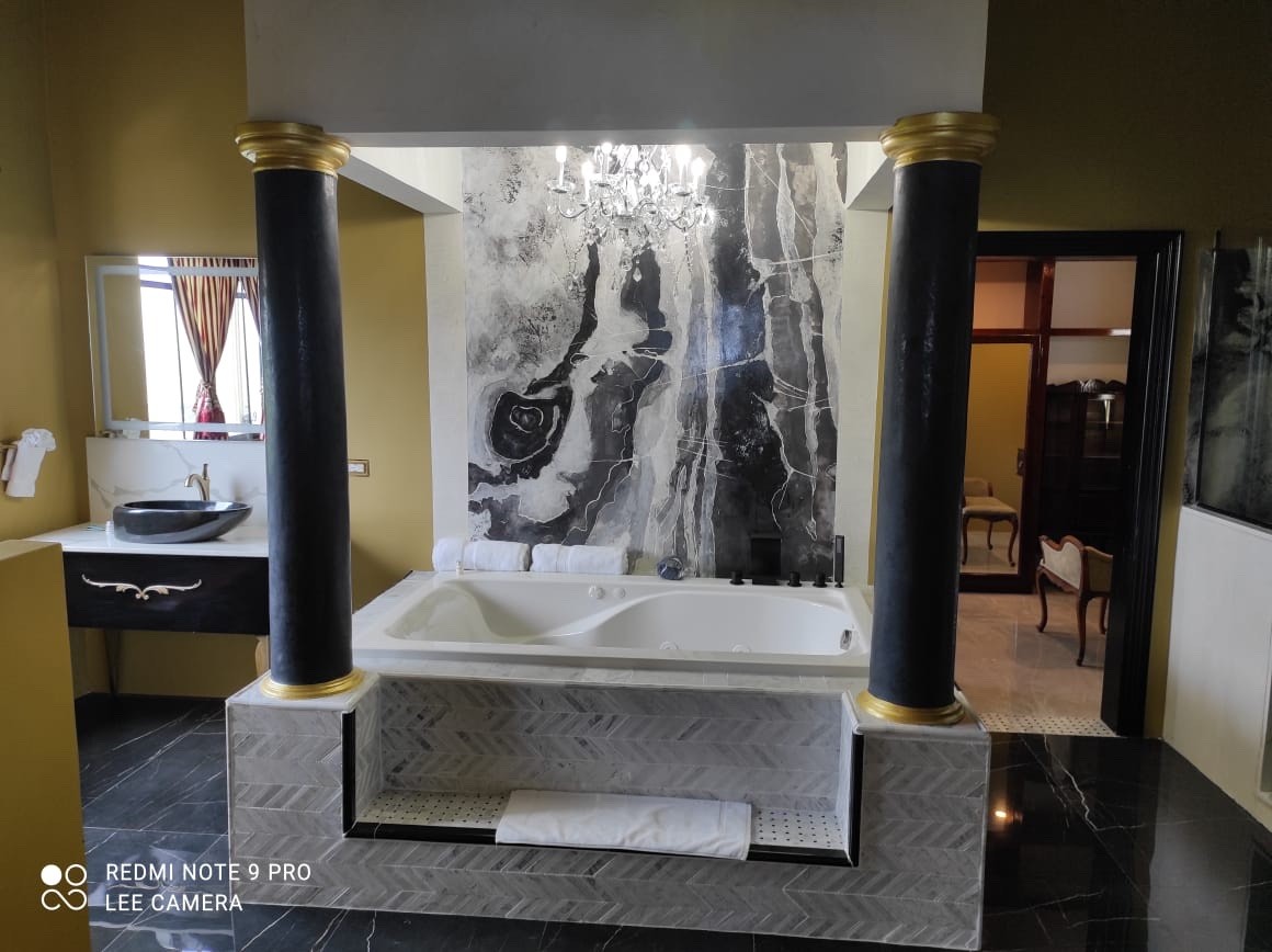 Villa Mimosa master bathroom with black Venetian plaster columns, gold capitals and a black-and-white marble-effect wall behind the bath.