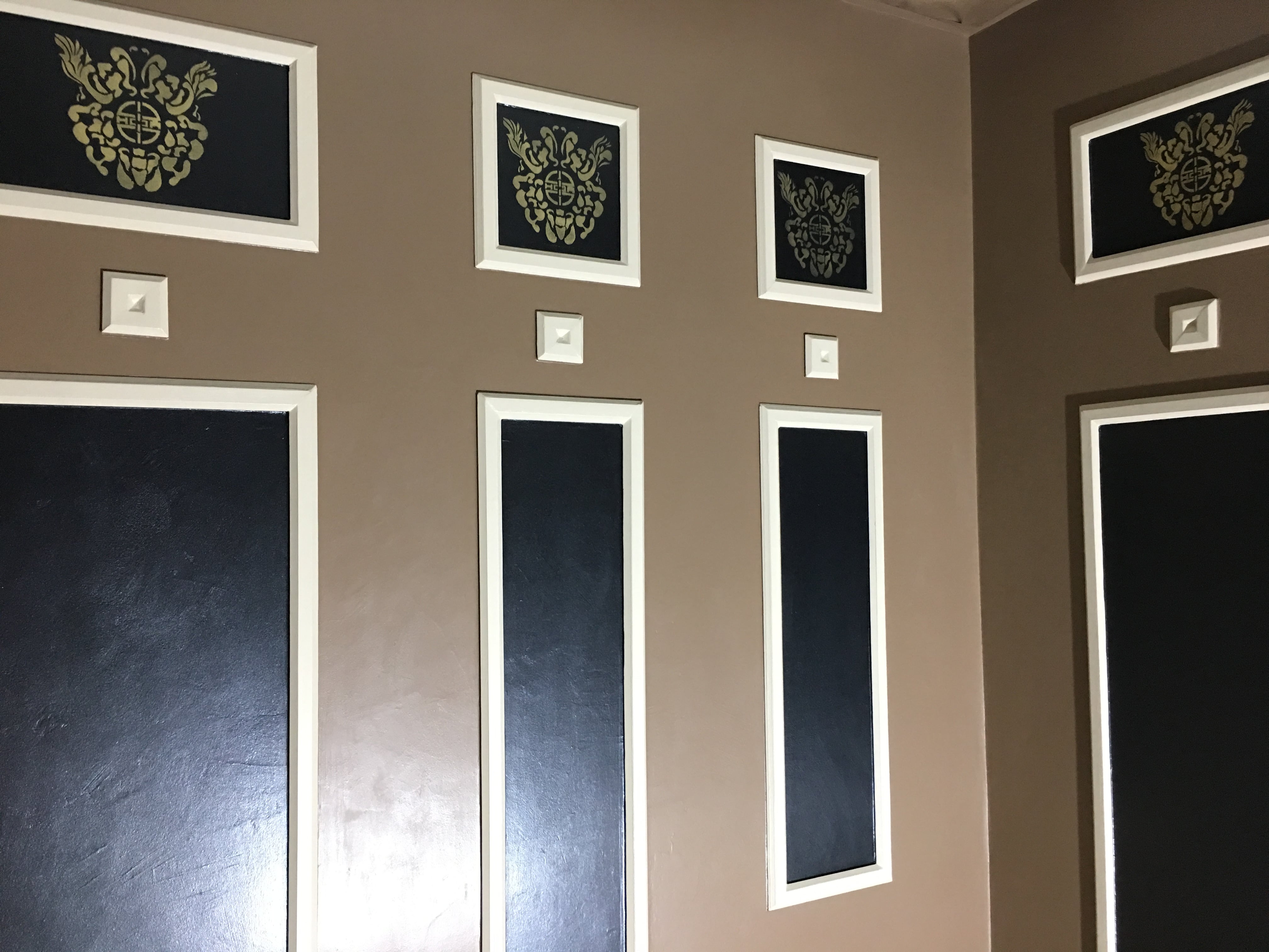 Finished custom stencils in the upper squares above the powder room’s dark rectangular panels and cream trim
