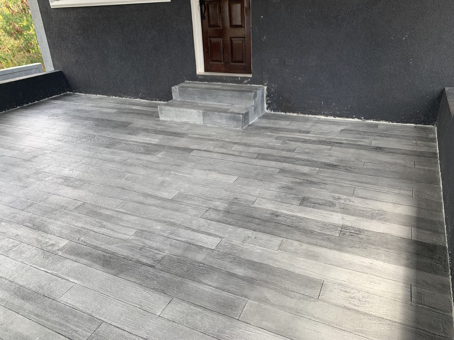 Grey woodgrain floor on a covered terrace with steps and daylight across the surface
